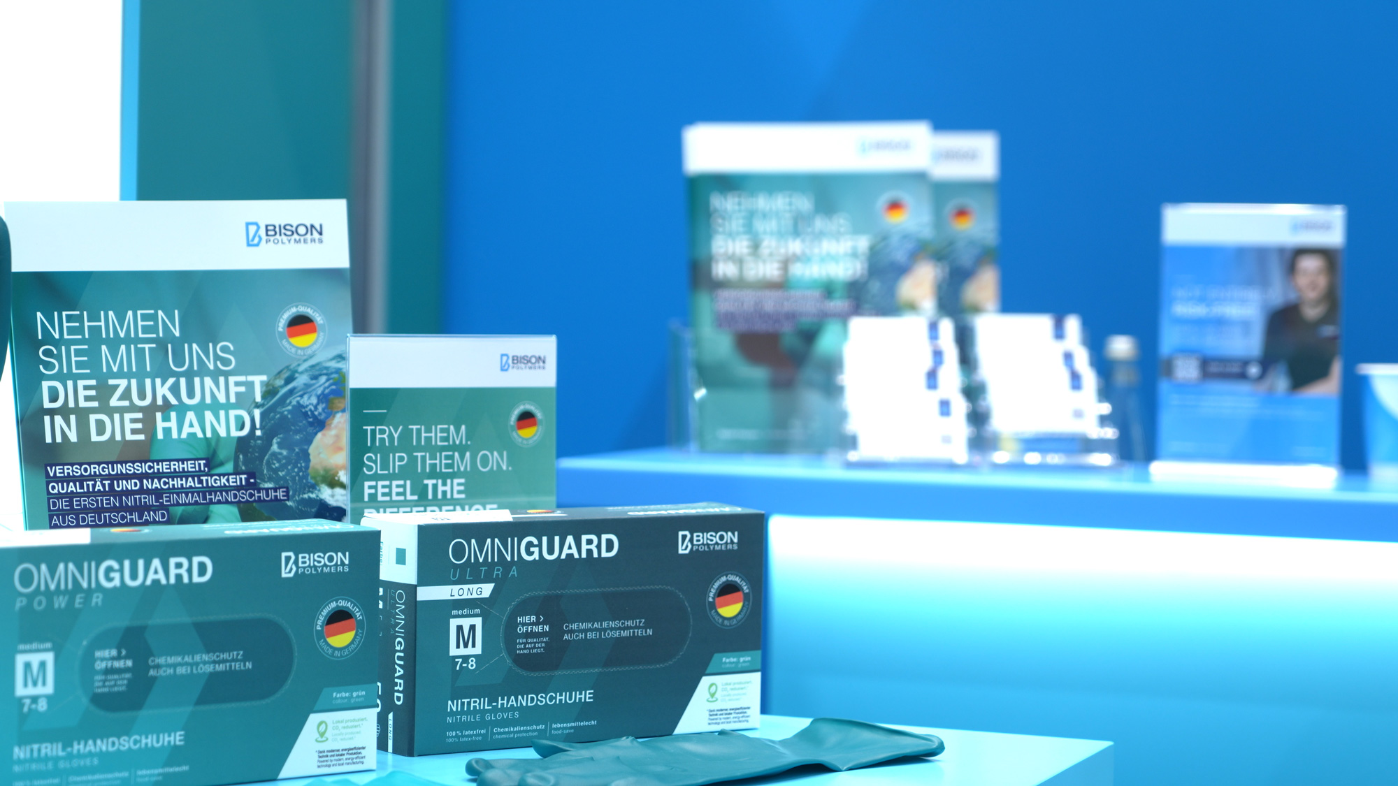 Präsentation der OMNIGUARD Nitril-Einmalhandschuhe von BISON Polymers auf der A+A. Die Darstellung betont Qualität, Schutz und Made-in-Germany-Produktion.