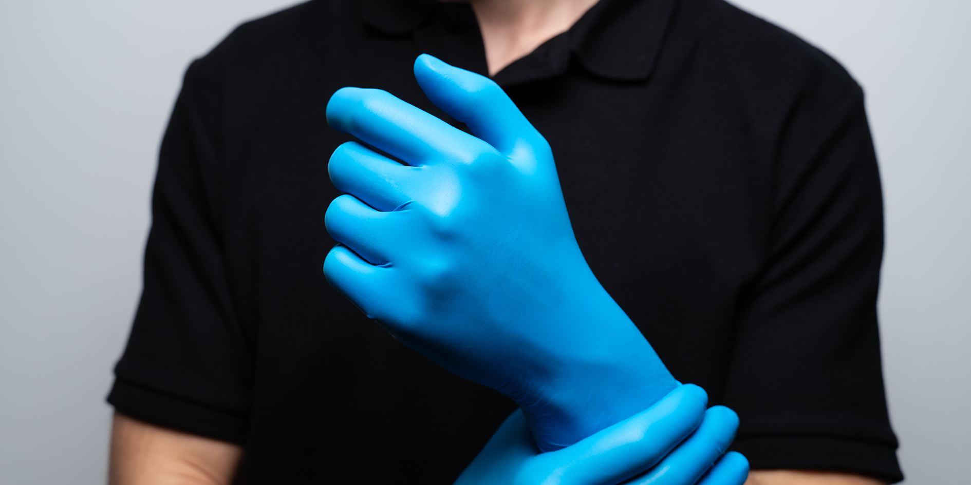 Close-up of hands wearing blue disposable gloves, linked in a clasp against a black shirt backdrop.